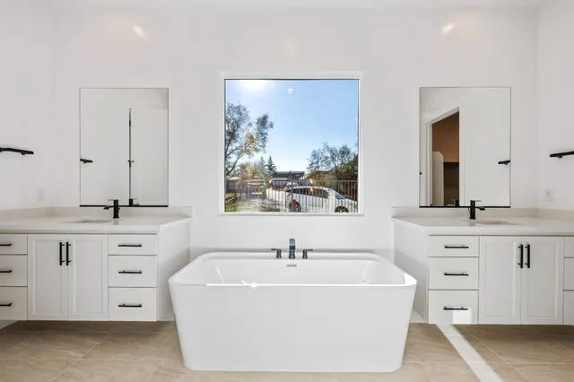a spacious bathroom with double vanity sink a two mirror a window a bathtub and vanity