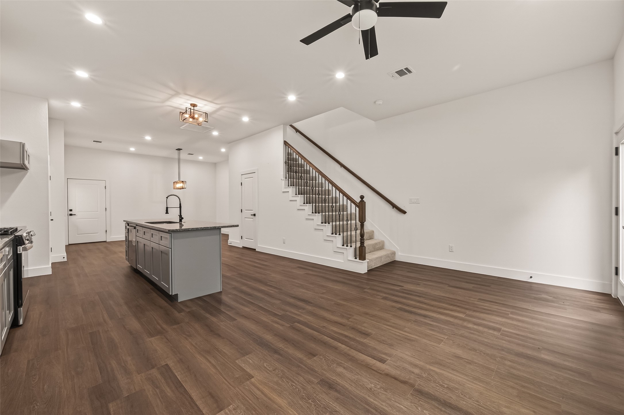 6808 Madrid Street Houston, TX 77021 - Photo 9 of 31 This spacious open-concept living area features sleek engineer wood floors, a modern kitchen island with a dark countertop, and a stylish ceiling fan. The area is well-lit with recessed lighting, and a staircase with wooden railings leads to the upper level, making it ideal for entertaining and comfortable living.