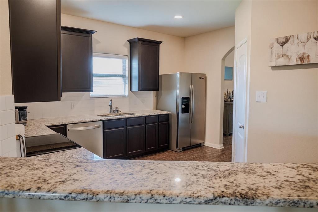 1837 Rialto Lane Crowley, TX 76036 - Photo 15 of 19 Kitchen featuring speckled countertops, dark wood cabinetry, stainless steel appliances, a white tile backsplash, and wood-finish flooring