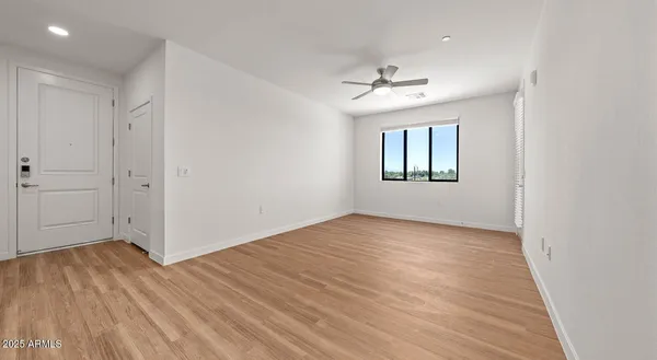 an empty room with wooden floor chandelier fan and windows
