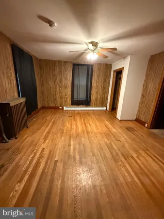 a view of an empty room with wooden floor and a ceiling fan