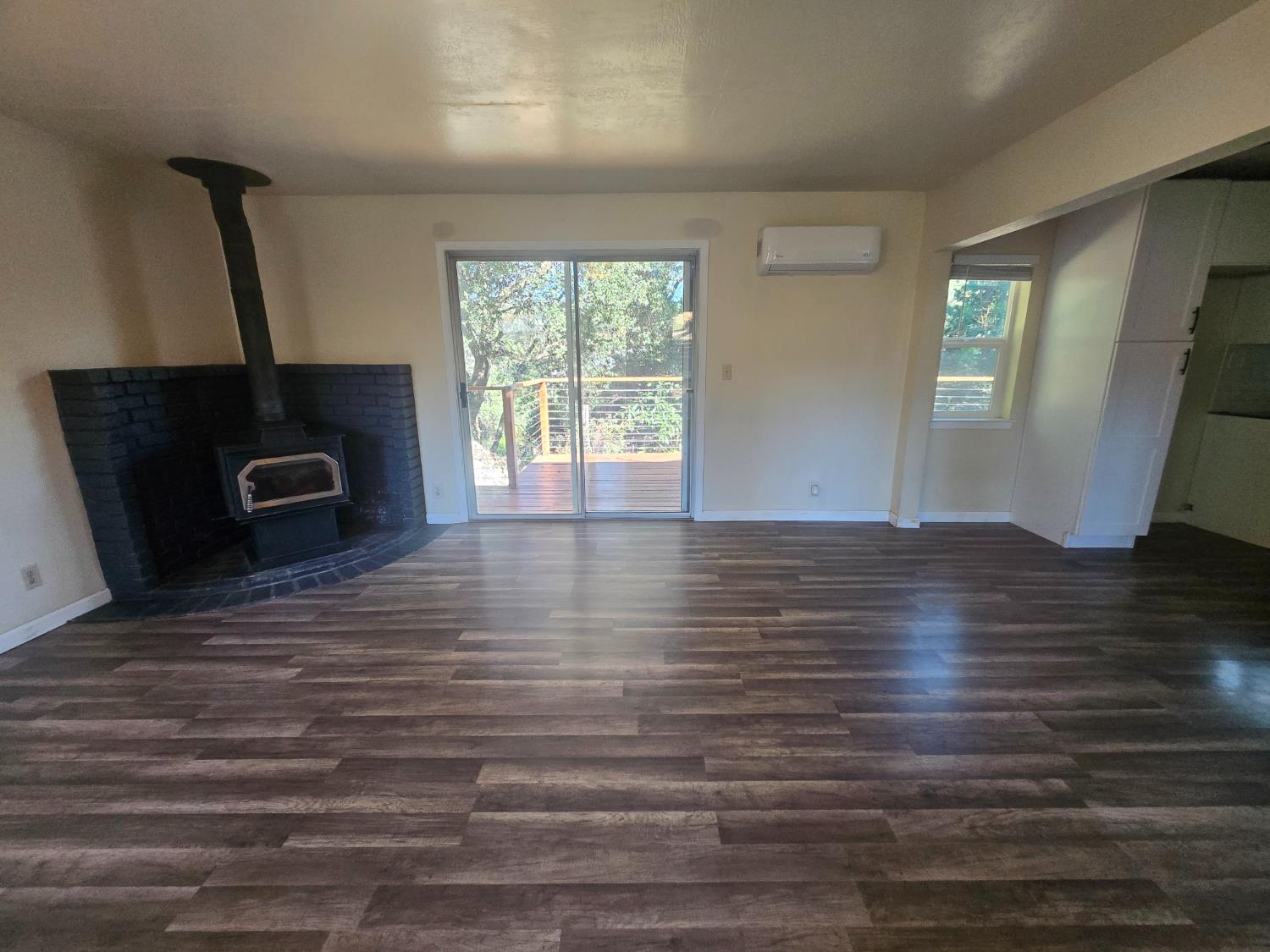 10601 Lime Kiln Road Grass Valley, CA 95949 - Photo 10 of 79 Spacious room featuring wood-finish flooring, a black brick fireplace with a wood-burning stove, and a sliding glass door opening to an outdoor deck