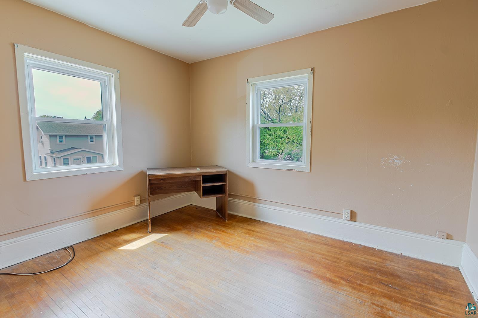 438 9th Street Cloquet, MN 55720 - Photo 23 of 27 Room featuring wood-finish flooring, two windows with white trim, and a ceiling fan
