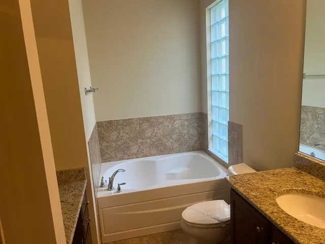 a bathroom with a granite countertop bathtub shower sink vanity and toilet