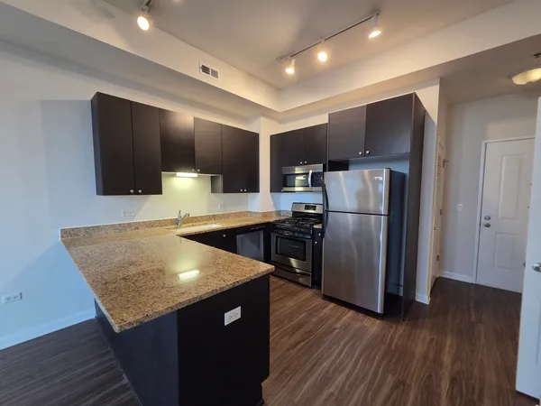 a kitchen with granite countertop a refrigerator a stove and wooden floor