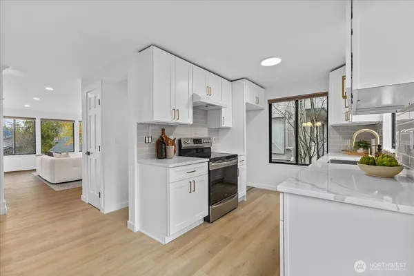 a kitchen with granite countertop a stove a sink a refrigerator and white cabinets with wooden floor