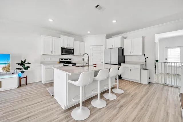 a kitchen with stainless steel appliances a stove top oven a refrigerator a sink and white cabinets with wooden floor