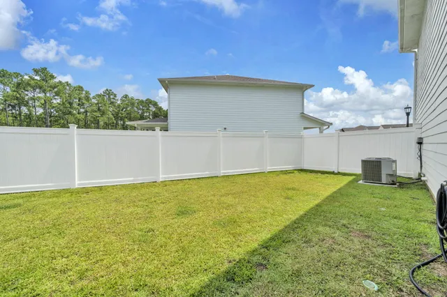 a view of a white house with a yard plants and large tree