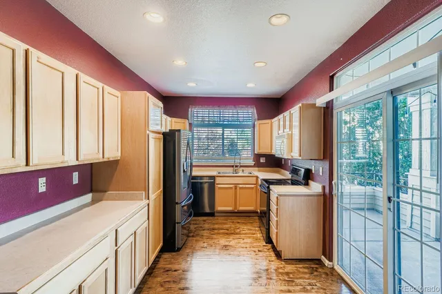 a kitchen with stainless steel appliances granite countertop a refrigerator a sink dishwasher a stove and a dining table with wooden floor