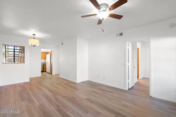 an empty room with wooden floor chandelier fan and windows