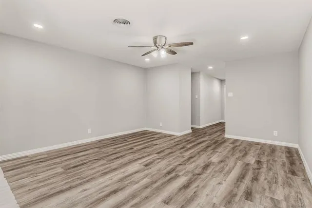 an empty room with wooden floor ceiling fan and kitchen view