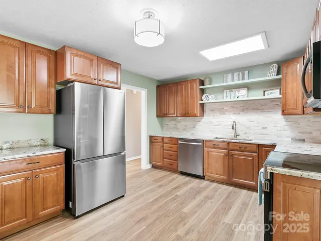 a kitchen with granite countertop stainless steel appliances a refrigerator a sink and wooden cabinets