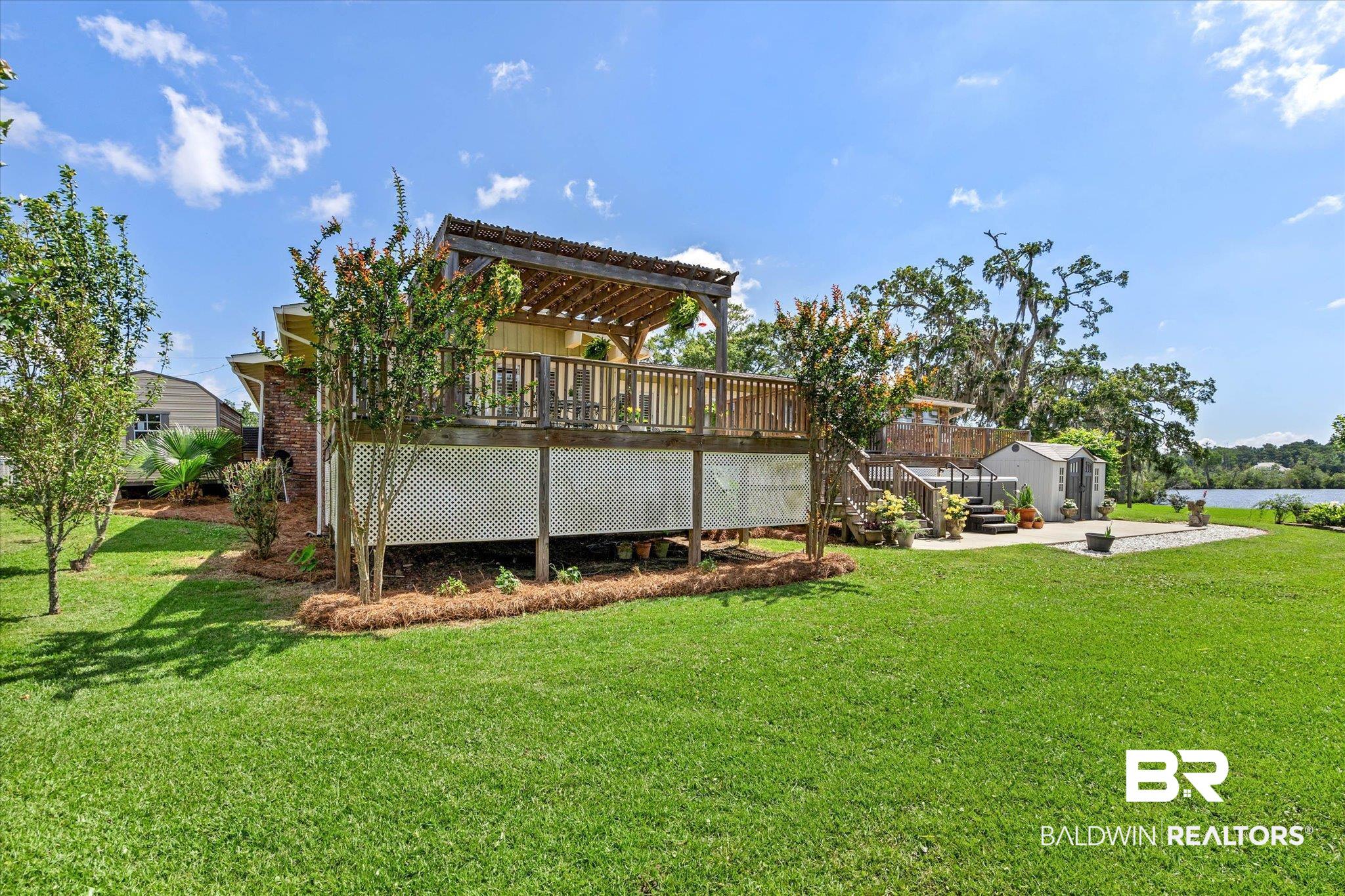 3801 Point Road Mobile, AL 36619 - Photo 38 of 55 Expansive backyard featuring a large green lawn, multi-level deck with pergola, brick exterior accents, a detached storage shed, and a body of water in the background