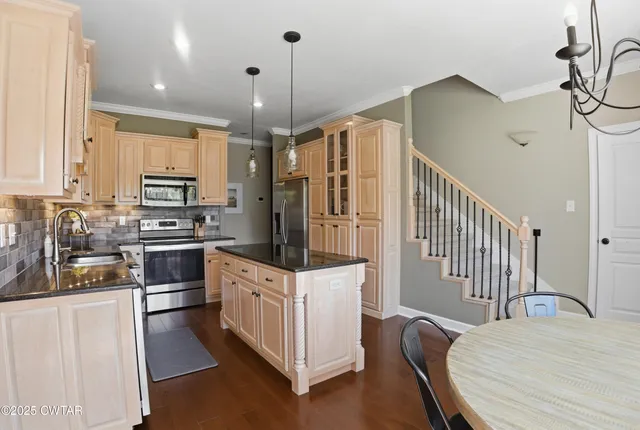 a kitchen with stainless steel appliances kitchen island granite countertop a refrigerator a stove a sink and white cabinets with wooden floor