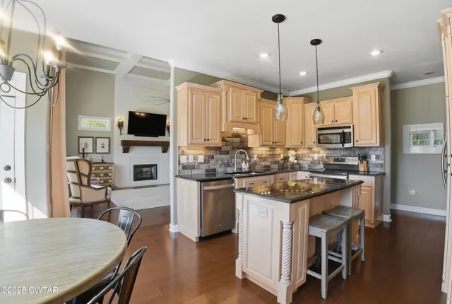 a kitchen with stainless steel appliances granite countertop a stove top oven a refrigerator a sink and chairs