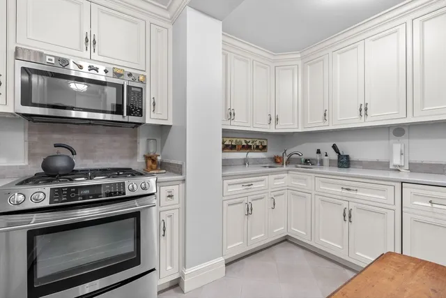 a kitchen with stainless steel appliances granite countertop grey cabinets a stove a sink and a microwave