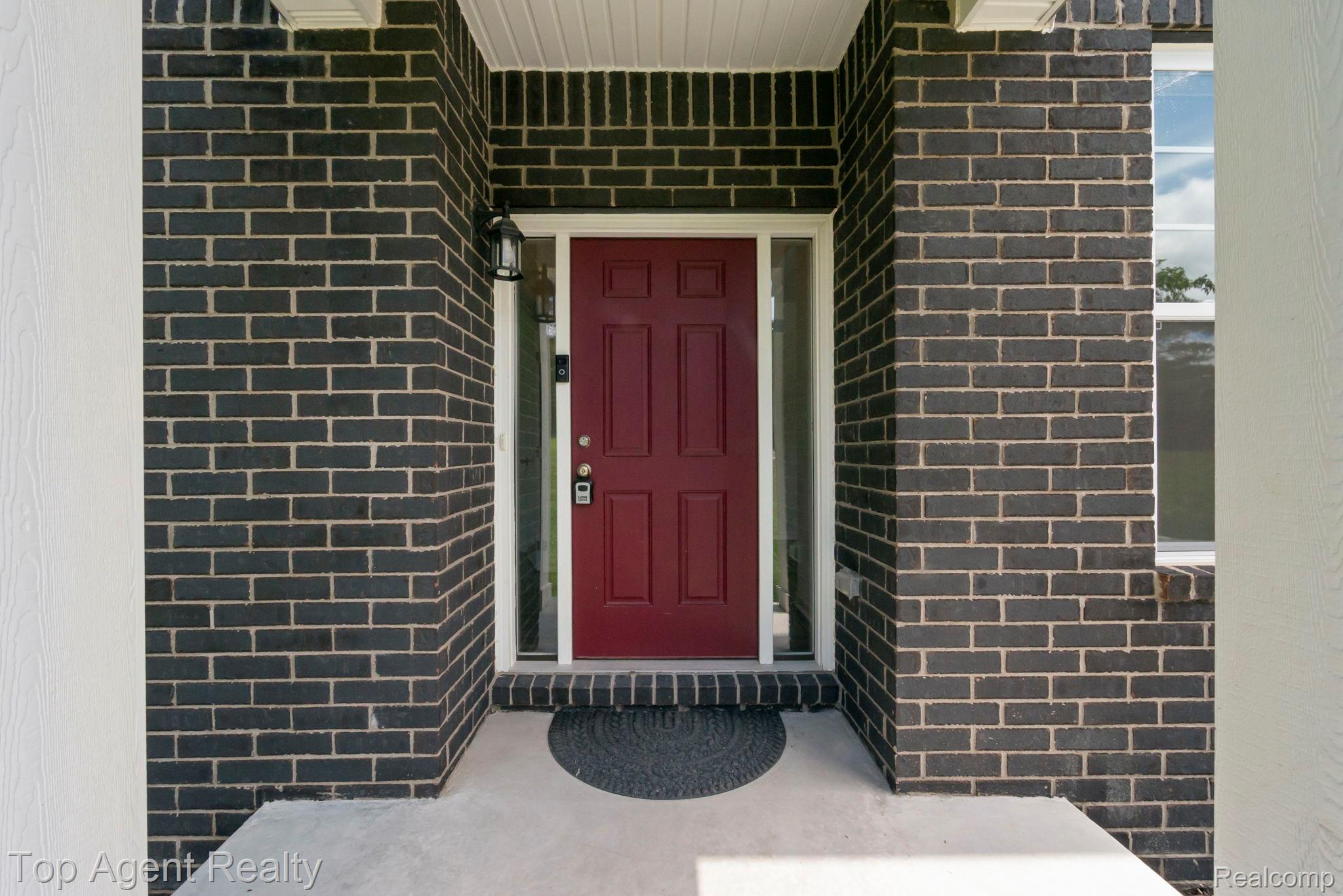 63770 Dequindre Road Washington, MI 48095 - Photo 52 of 61 Inviting entry featuring a deep red door with transom window and sidelights, set against dark brickwork