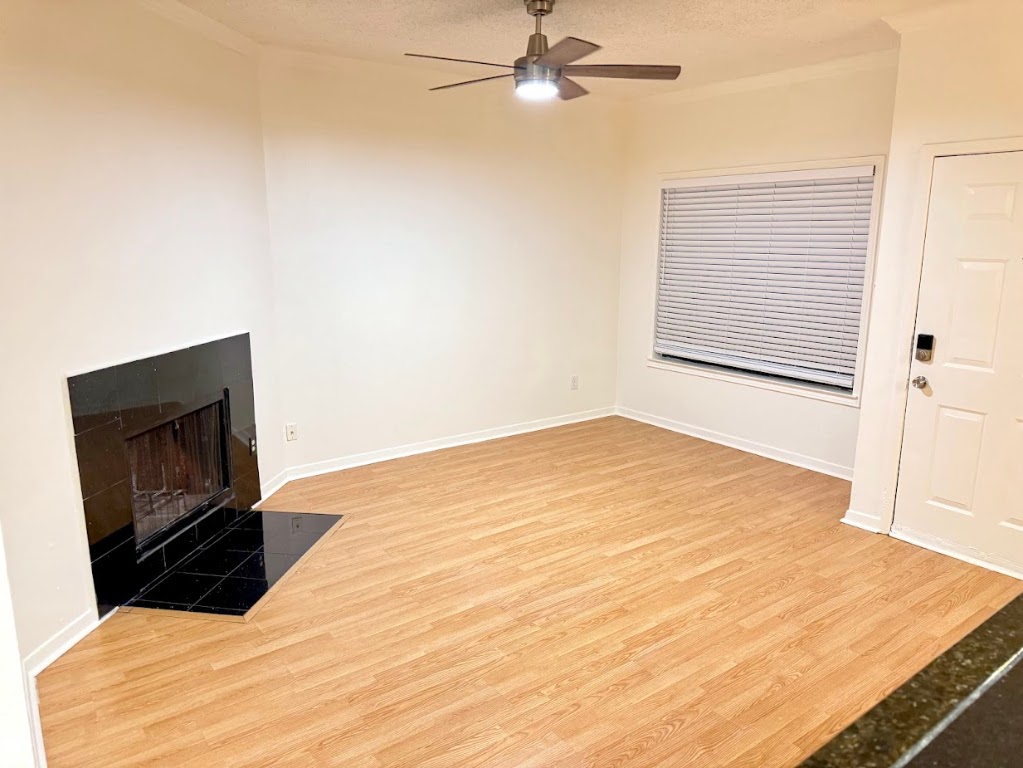 915 West 23rd Street, Unit 108 Austin, TX 78705 - Photo 5 of 15 Unfurnished living room featuring a tile fireplace, light wood-style floors, a textured ceiling, ceiling fan, and crown molding
