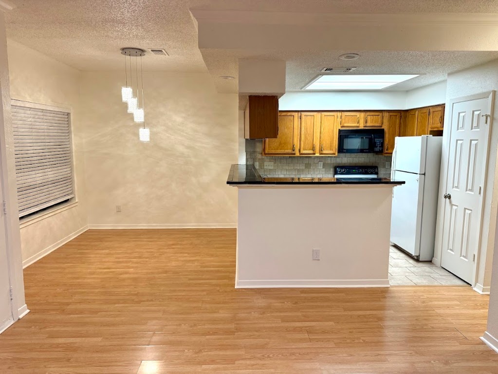 915 West 23rd Street, Unit 108 Austin, TX 78705 - Photo 6 of 15 Kitchen with dark countertops, brown cabinetry, decorative light fixtures, black appliances, and a textured ceiling