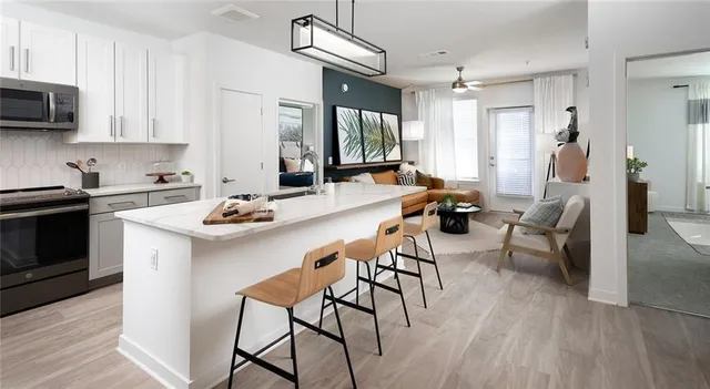 a kitchen with stainless steel appliances kitchen island granite countertop a stove a sink a refrigerator and white cabinets with wooden floor