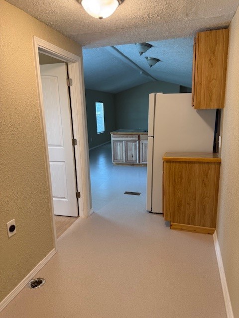 22786 Cuttler Road New Caney, TX 77357 - Photo 8 of 12 This photo shows a utility room leading to a spacious living area with high ceilings. There's a small kitchen visible with wooden cabinets and a refrigerator. The walls are neutral, and the space is well-lit with ceiling lights.
