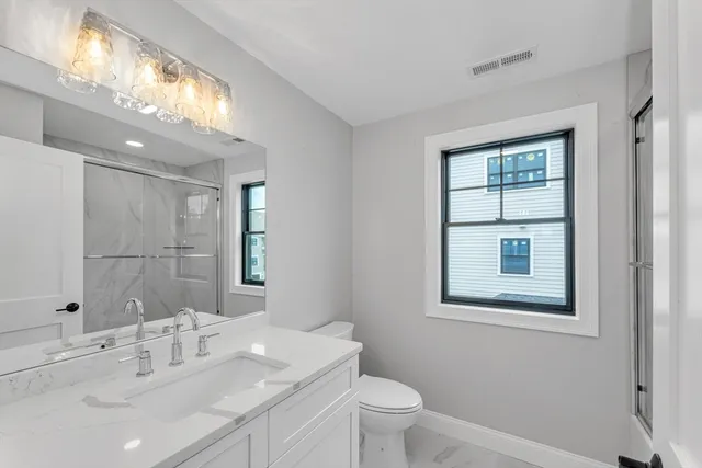 a bathroom with a toilet a sink a mirror and a window