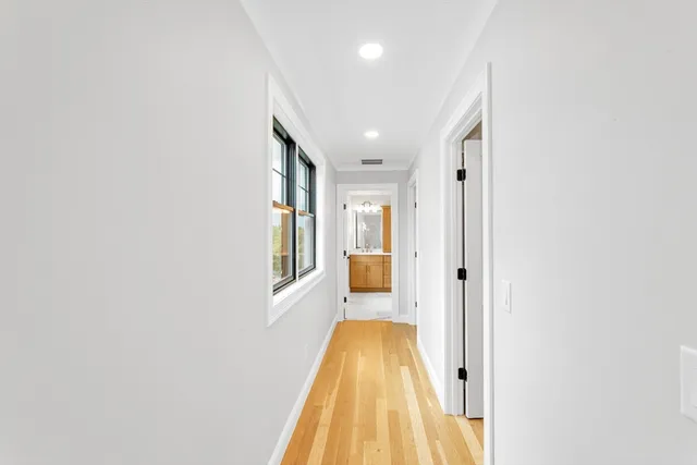 a view of a hallway with wooden floor and a bathroom