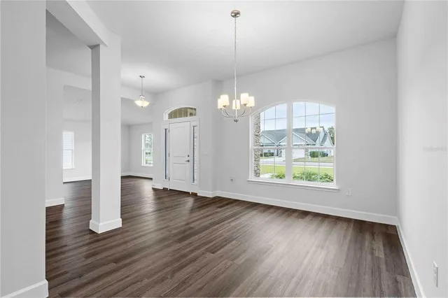 an empty room with wooden floor chandelier and windows