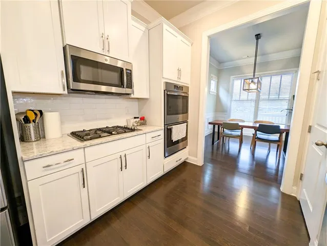 a kitchen with stainless steel appliances granite countertop a refrigerator a stove top oven a sink dishwasher and white cabinets with wooden floor