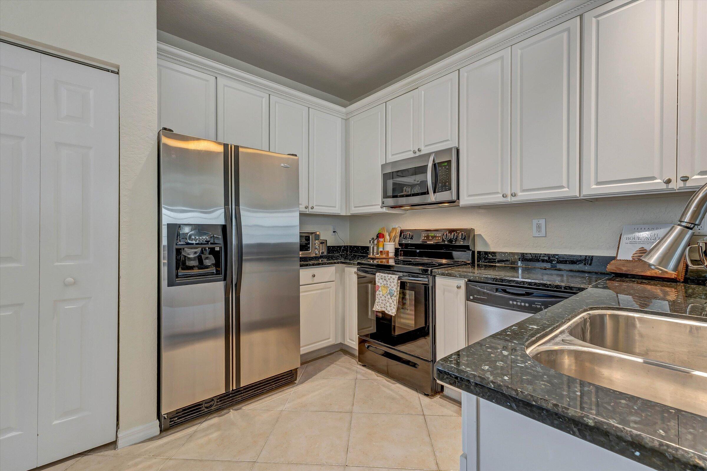 115 Pond Apple Lane, Unit 105 Jupiter, FL 33458 - Photo 12 of 38 a kitchen with granite countertop a refrigerator stove and microwave
