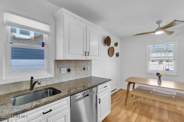 a kitchen with a sink dishwasher and white cabinets with wooden floor