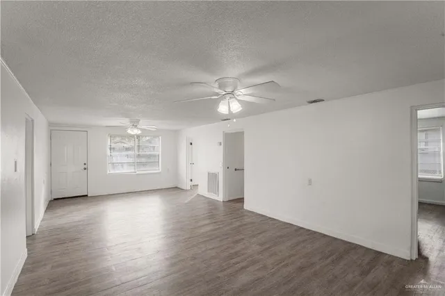 an empty room with wooden floor chandelier fan and windows