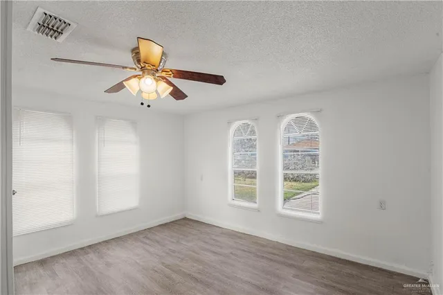 an empty room with wooden floor fan and windows
