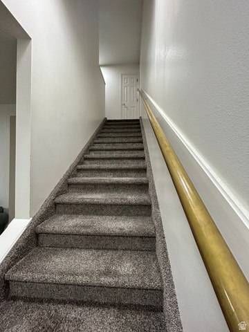 203 North Geneva Road, Unit 10 Provo, UT 84601 - Photo 10 of 16 Carpeted staircase featuring a light wood-finish handrail, white trim, and a paneled door at the landing