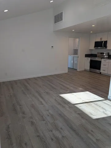 an empty room with wooden floor and kitchen view