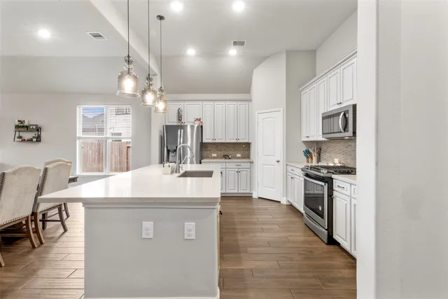 a large kitchen with stainless steel appliances kitchen island granite countertop a stove a sink a refrigerator a dining table and chairs with wooden floor