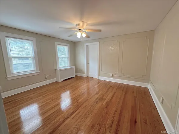 an empty room with wooden floor chandelier fan and windows