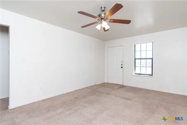 an empty room with a chandelier fan and windows