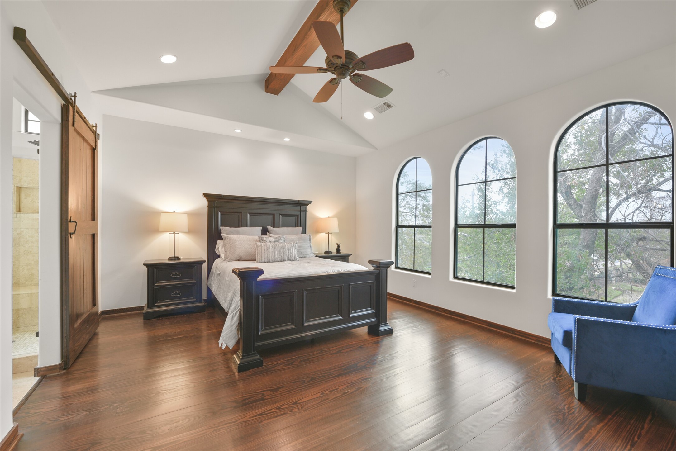 2601 Bevis Street, Unit B Houston, TX 77008 - Photo 14 of 25 The Primary bedroom is located on the 3rd floor with another secondary bedroom and overlooks the backyard. Boasts a vaulted ceiling with a rustic wood beam and ceiling fan, plus oversized windows that fill the space with natural light. A cozy study nook with built-in countertop/desk (not shown here) and recessed can lighting makes it a perfect retreat. A sliding stained wood barn door leads to the en suite primary bath, adding a touch of character.