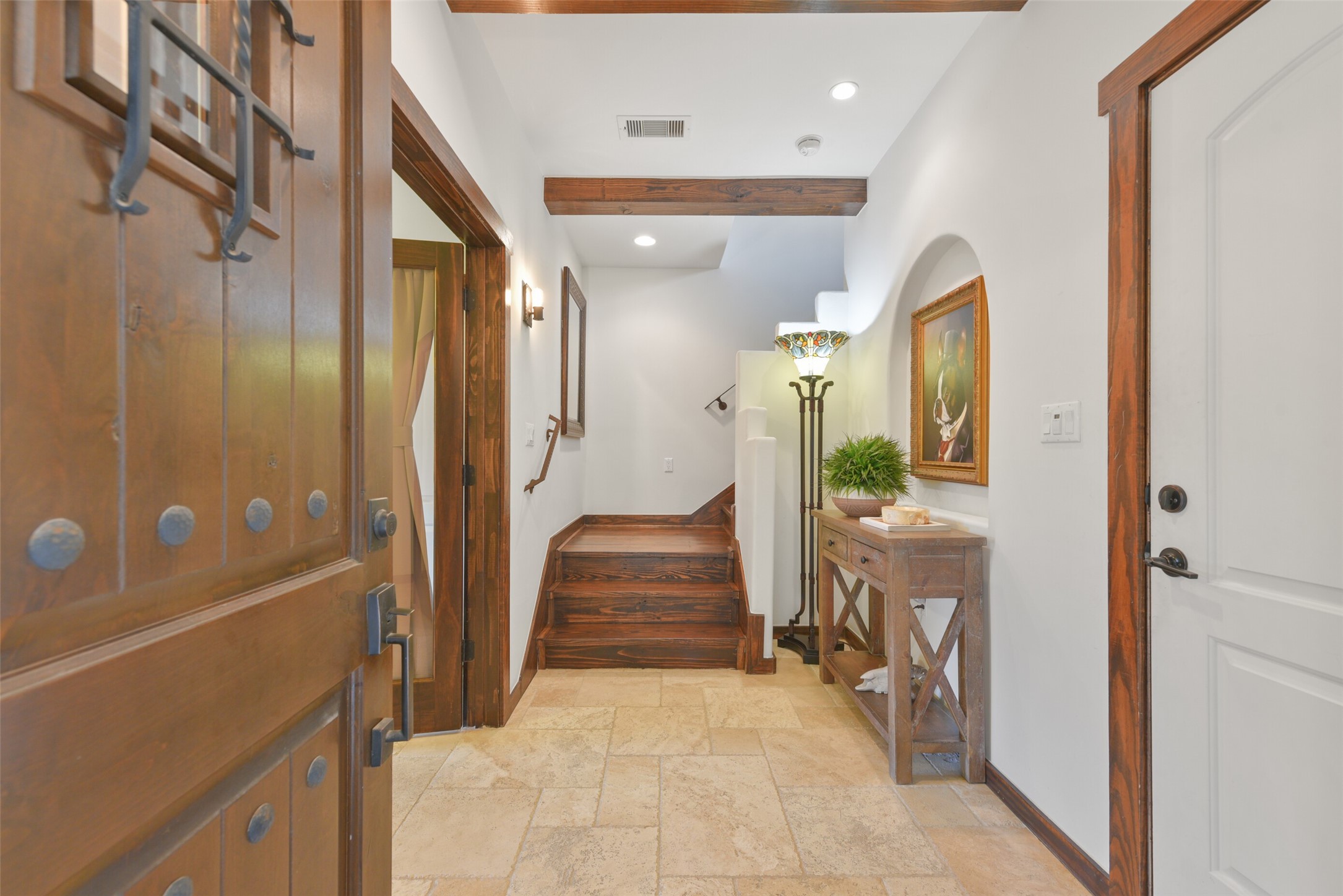2601 Bevis Street, Unit B Houston, TX 77008 - Photo 2 of 25 Welcoming entry with Mediterranean-style hardwood front door and room for an entry table. The space is illuminated by recessed can lights, highlighting the elegant art niche and large tile travertine floors. A stunning wood beam ceiling detail adds character, while the hardwood stairs with iron railings lead to the upper levels. Convenient door access to the attached garage completes this thoughtfully designed entry.