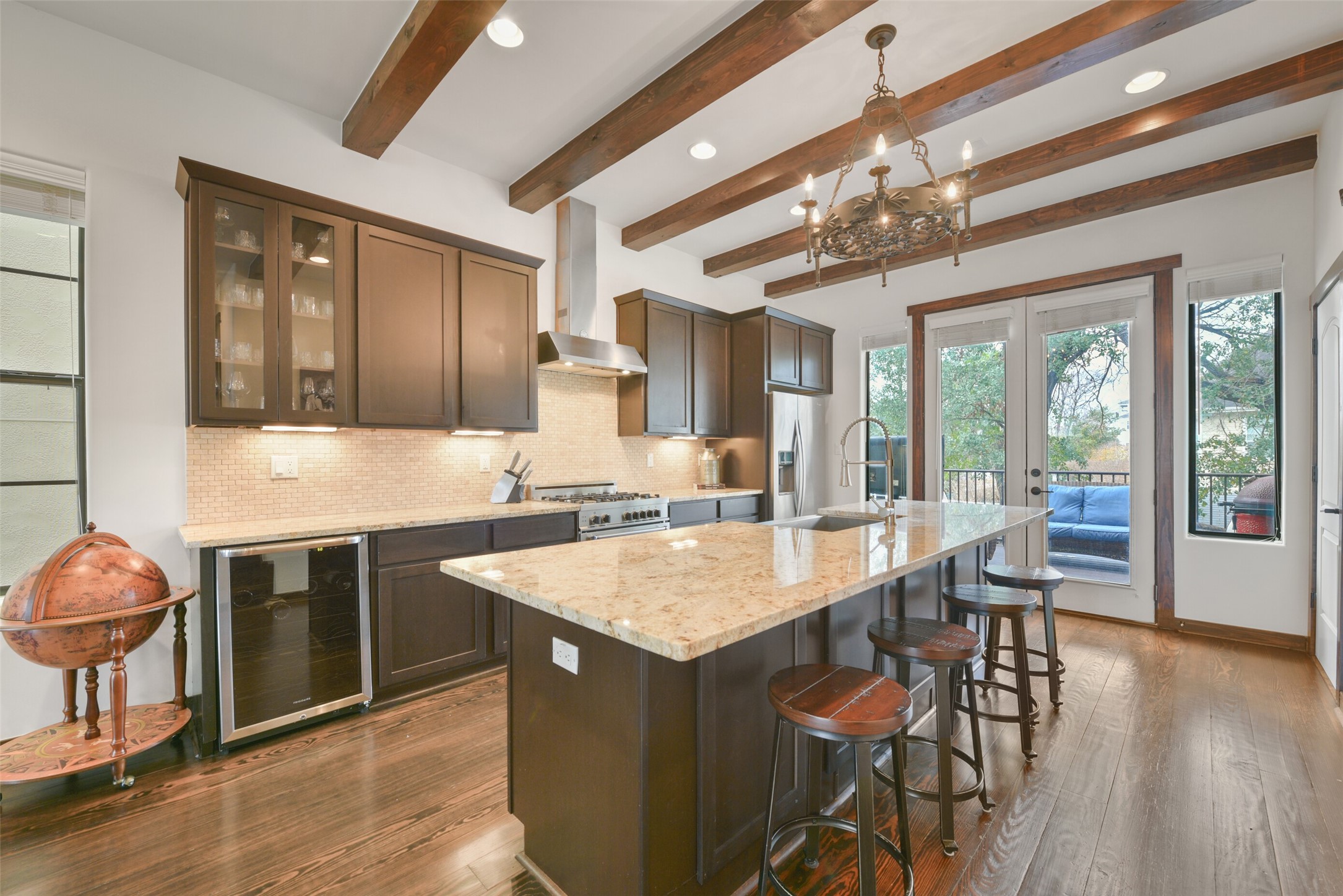 2601 Bevis Street, Unit B Houston, TX 77008 - Photo 7 of 25 Stunning chef’s kitchen with rustic wood ceiling beams and an open layout that flows into the dining and living areas, ideal for entertaining. Features include granite countertops, a travertine tile backsplash, and an expansive 8’ island with breakfast seating with a decorative chandelier. Plenty of cabinet space make this a dream space for cooking and hosting. A door leads to the extended patio for seamless indoor-outdoor living.