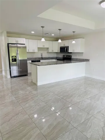 a large white kitchen with kitchen island granite countertop a large counter top and stainless steel appliances