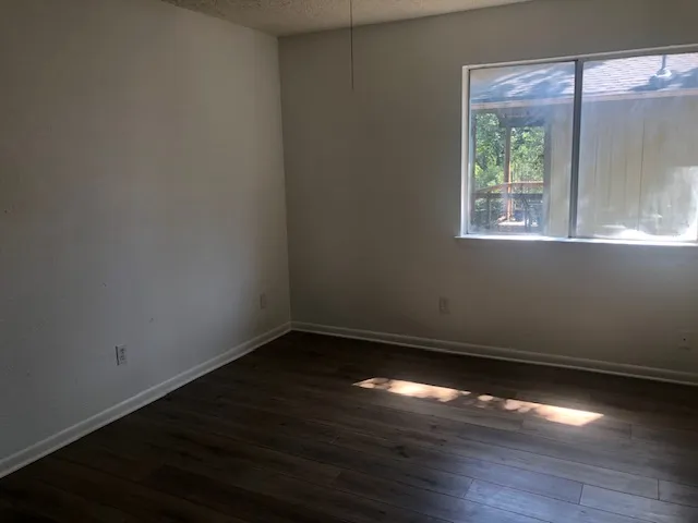 a view of an empty room with wooden floor and a window