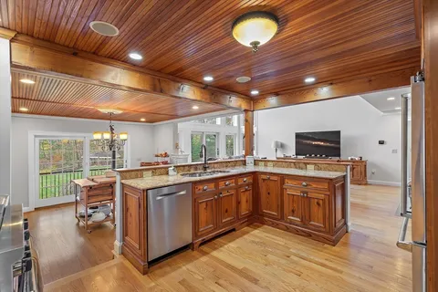 a kitchen with stainless steel appliances granite countertop wooden cabinets a sink dishwasher a dining table and chairs with wooden floor