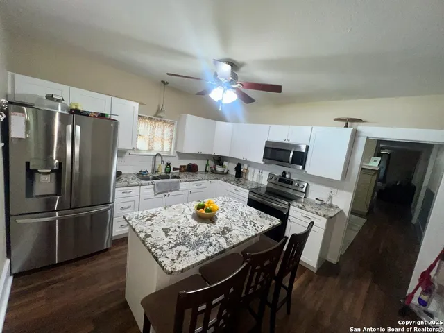 a kitchen with stainless steel appliances granite countertop a dining table chairs refrigerator and microwave