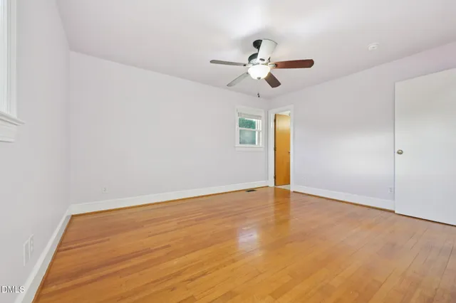 an empty room with wooden floor ceiling fan and windows