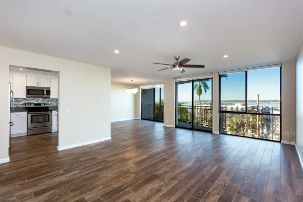 a view of an empty room with wooden floor and a kitchen