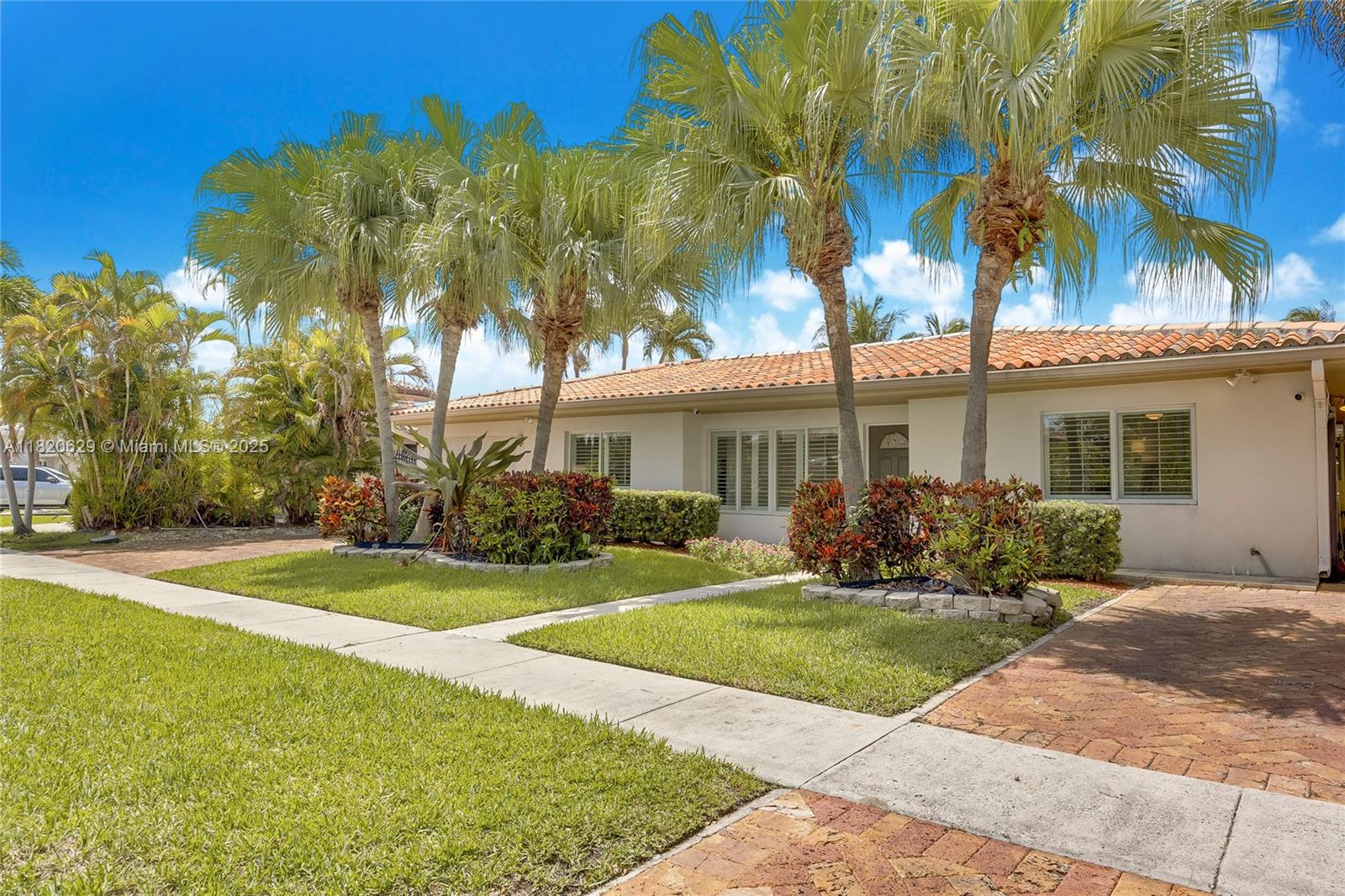 a view of a white house with a big yard and potted plants and palm trees