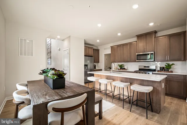 a large white kitchen with stainless steel appliances kitchen island granite countertop a dining table chairs and white cabinets