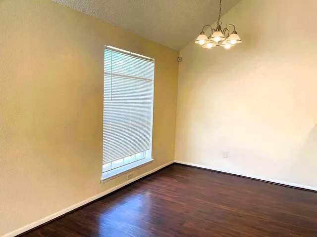 an empty room with wooden floor chandelier and window